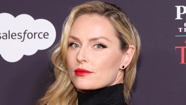 Lindsey Vonn poses in a black high-neck dress and a red lip and looks at the camera.