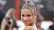 Rose Bertram wears a slicked-back high bun and smiles over her shoulder at the camera.