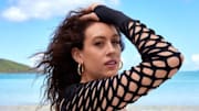 Breanna Stewart stands in front of the bright blue ocean in a black long-sleeve bathing suit with cut-outs.