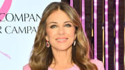 Elizabeth Hurley smiles at the camera, wearing a pink dress and diamond drop earrings.