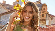 Olivia Ponton poses in a green one-shoulder one-piece swimsuit in front of the stone buildings in Montenegro.