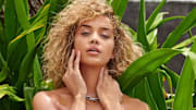 Jasmine Sanders poses in front of vibrant green leaves wearing a silver chain necklace.