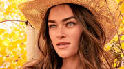 Myla Dalbesio poses in front of the bright yellow leaves in a tan straw cowgirl hat.
