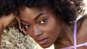 Tanaye White lounges on the ground in a purple bikini and leans her head on her