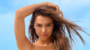 Alexis Ren poses with her arm above her head and smiles for the camera.