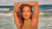 Mia Kang poses in front of the ocean in a crocheted bikini top and holds her arms above her head.