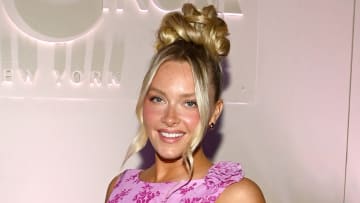 Camille Kostek poses in a pink floral-printed dress and wears her blonde hair in a high bun.
