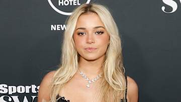 Olivia Dunne poses in a black lace dress and silver necklace in front of a black background.