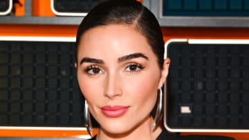Olivia Culpo smiles for the camera sporting a pink glossy lip, slicked-back hairdo and oversized silver earrings.