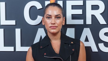 Lorena Durán poses in a black dress with silver zipper detailing and an collared neckline and wears her hair in a slicked-back updo.