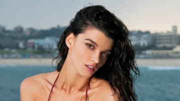 Crystal Renn poses in a red bikini and wet hair before the skyline of a beachside town in Australia.