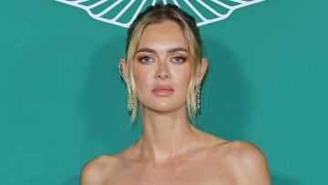 Megan Williams poses in front of a teal backdrop in diamond drop earrings and a messy up-do.
