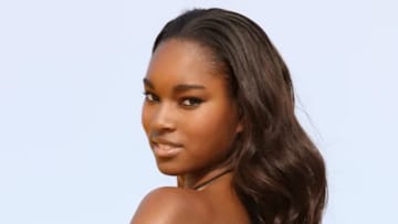 Damaris Lewis poses with her hair in a soft wave and smiles over her shoulder.