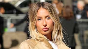 Alix Earle poses for the camera in a tan jacket and white tee.