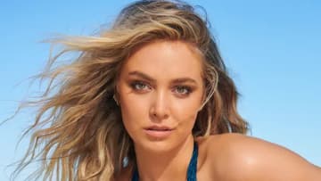 Raine Michaels poses in a blue halter neck swimsuit in front of the bright blue sky.