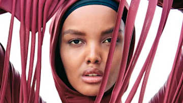 Halima Aden poses in berry pink hijab with long fringe hanging in front of her face.