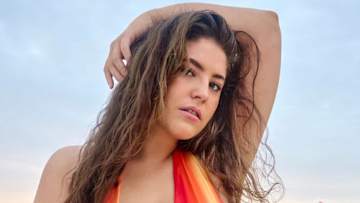 Gigi Robinson poses in a red and orange bikini with her arm over her head.