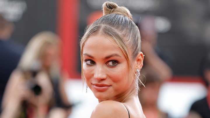 Rose Bertram wears a slicked-back high bun and smiles over her shoulder at the camera.