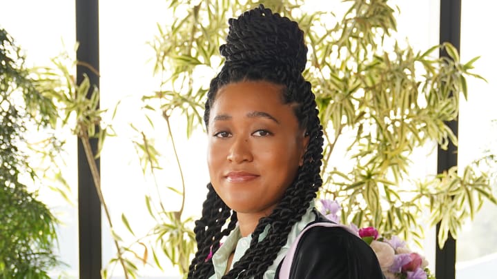 Naomi Osaka wears her hair in a bun on top of her head and smiles at the camera.