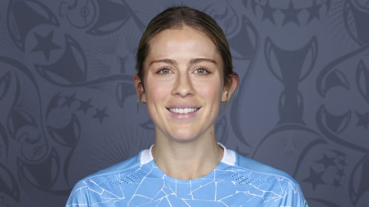 Abby Dahlkemper wears a blue soccer jersey and smiles for the camera.