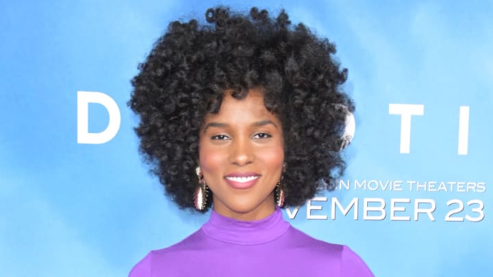 Drew Dorsey poses in a purple high-neck silk dress in front of a blue backdrop.