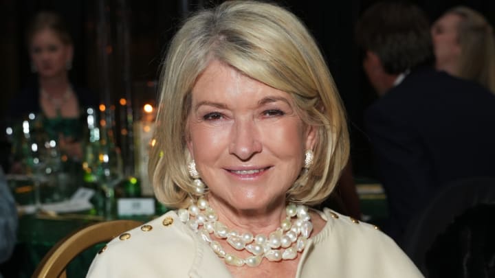 Martha Stewart wears a white coat and pearl necklaces and smiles for the camera.