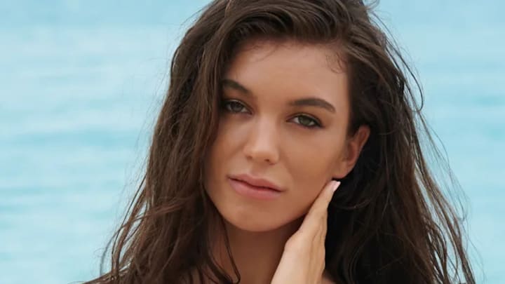 Erin Willerton poses in front of the ocean and looks at the camera.