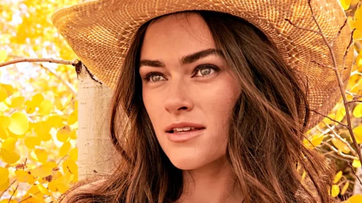 Myla Dalbesio poses in front of the bright yellow leaves in a tan straw cowgirl hat.