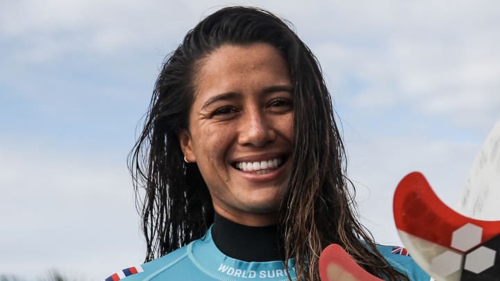 Malia Manuel poses in a blue surf shirt and wet hair and smiles at the camera. Malia Manuel poses in a blue surf shirt and wet hair and smiles at the camera.