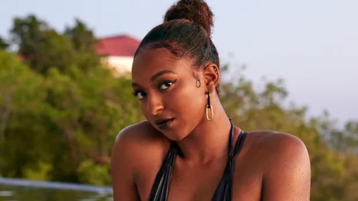 DiDi Richards poses in a black one-piece and full moody glam on the edge of a pool.
