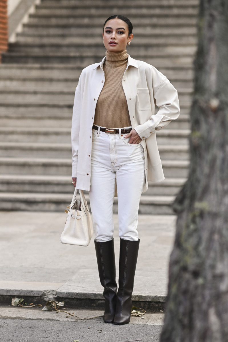 Kelsey Merritt is seen wearing a Hermes white jacket, tan turtleneck sweater, white pants and brown belt, brown boots and white Hermes bag outside the Hermes show during Paris Fashion Week.
