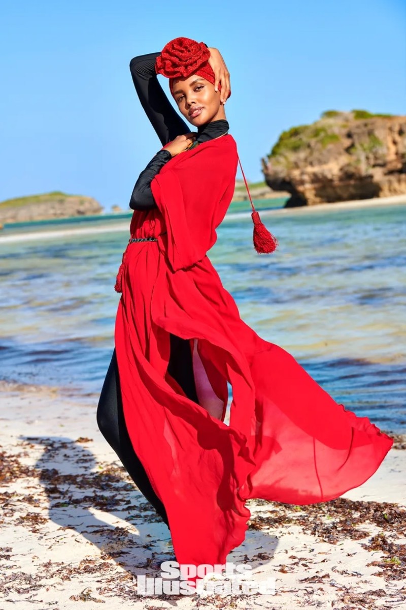 Halima Aden poses on the sand in a black catsuit, red kimono and red turban with floral detailing.