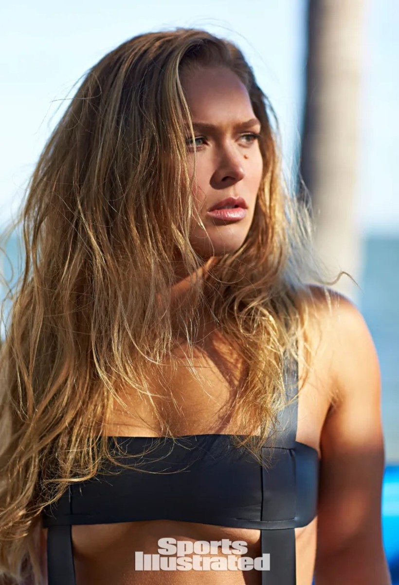 Ronda Rousey poses with her hair down in a black one-piece with cut-outs.