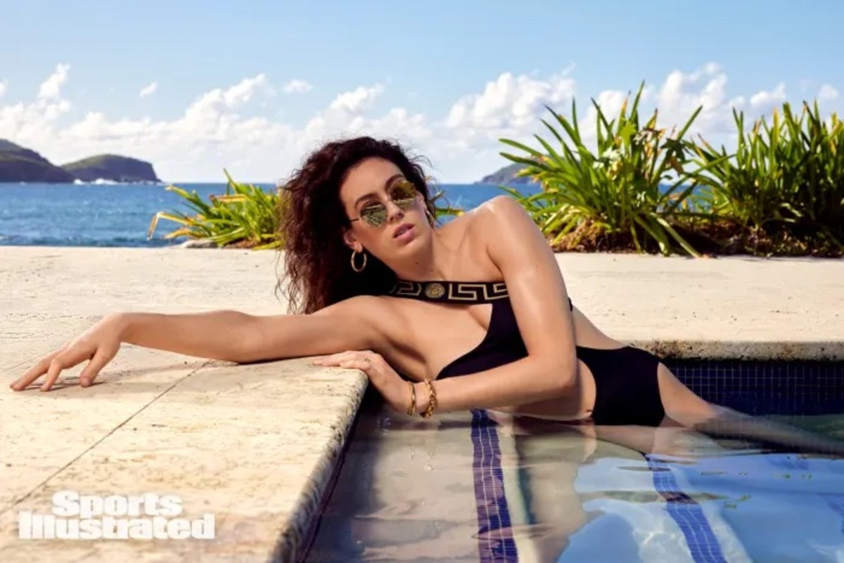 Breanna Stewart lays on the steps of the pool in a black Versace swimsuit.