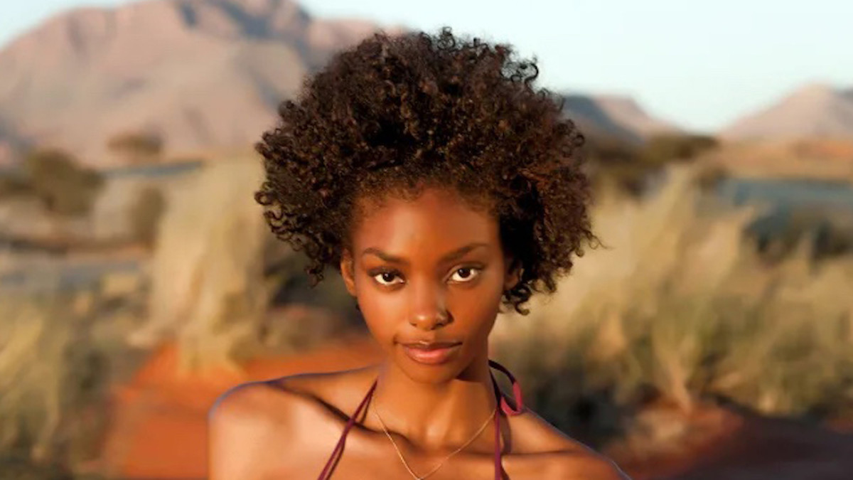 Adaora poses in a pink bikini in front of the scenic mountains and high grass of Namibia.