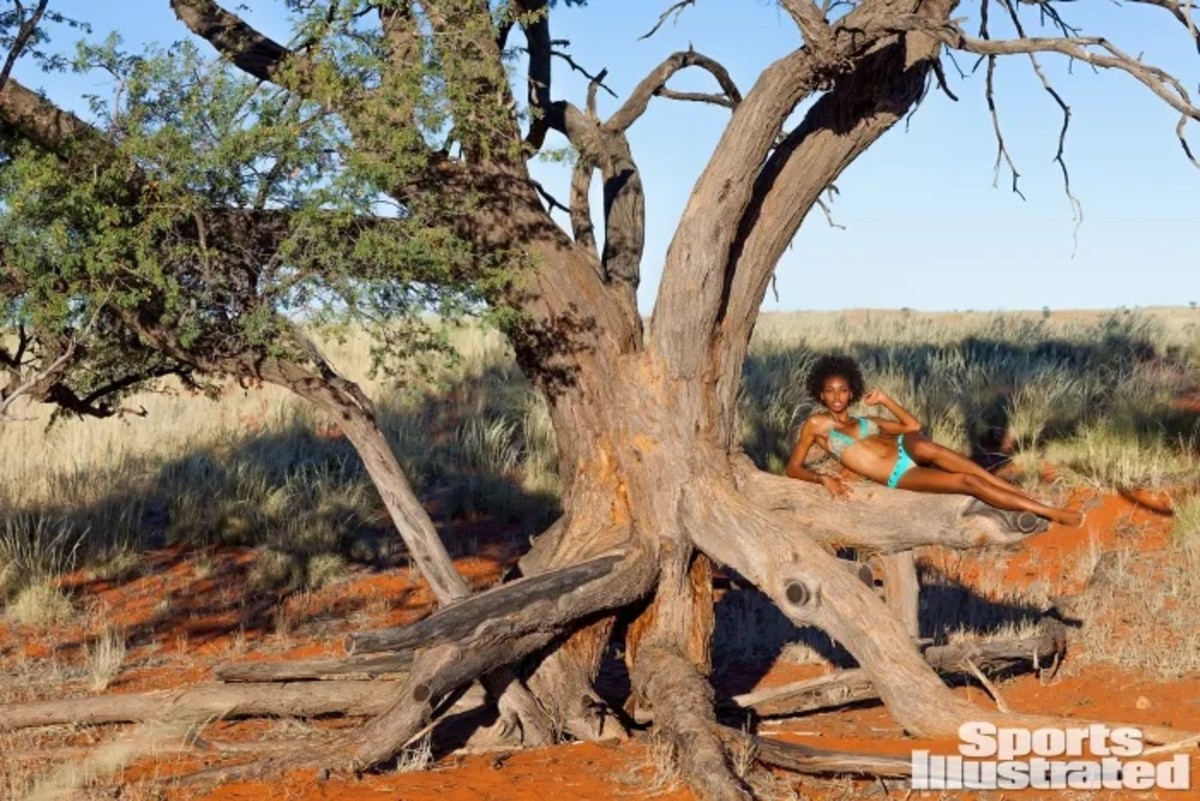 Adaora lounges on the trunk of a large tree in a bright blue bikini.