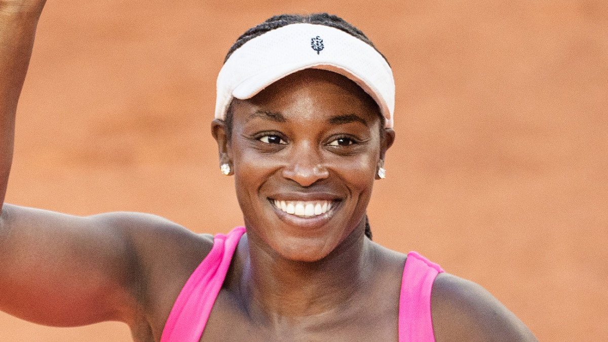 Sloane Stephens smiles and waves following a clay court match in a hot pink tennis dress and a white visor.
