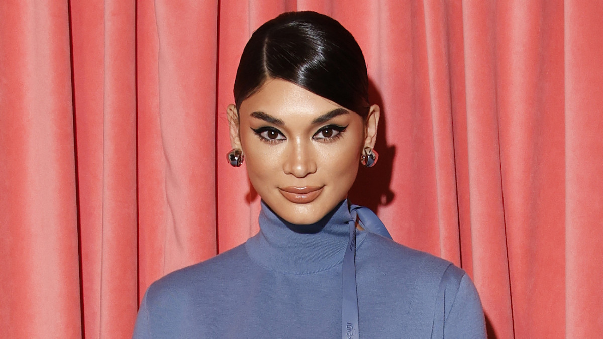 Pia Wurtzbach poses in a blue knit turtleneck dress and a slicked-back updo in front of a neon pink curtain.