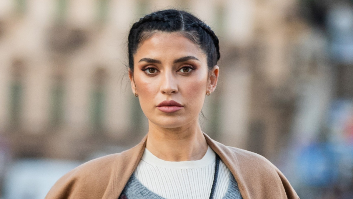 Nicole Williams English poses on the street in a white sweater and a tan coat. She wears her black hair in a braided updo.