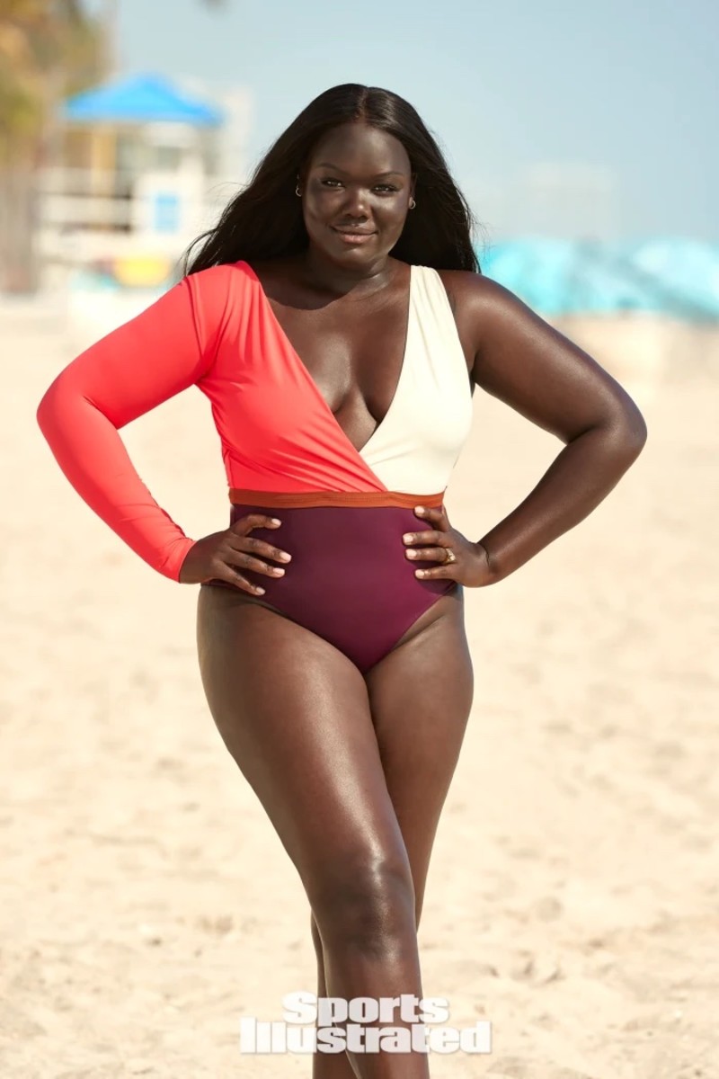 Nyma Tang poses on the sand in a salmon, white and berry color block one-piece.