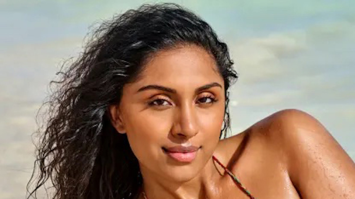 Manju lays on the beach in front of the ocean in a string bikini.