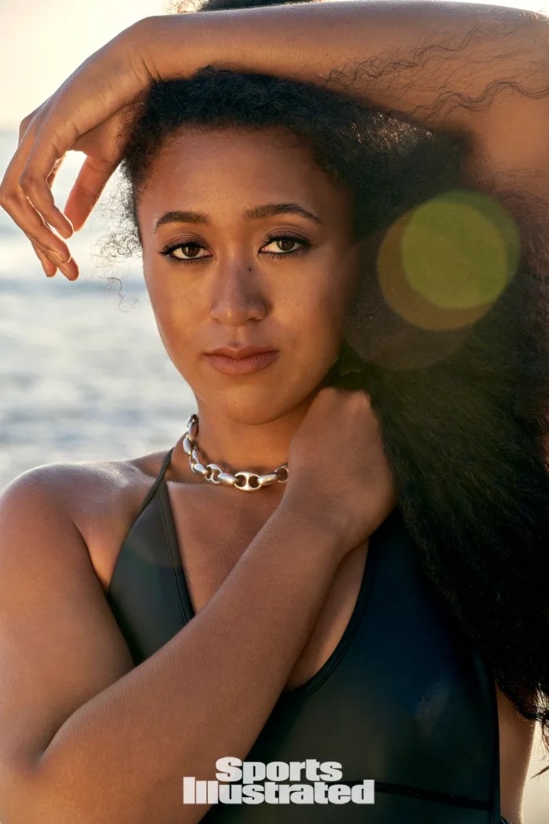 Naomi Osaka poses in a black bikini and silver necklace with her arm above her head.