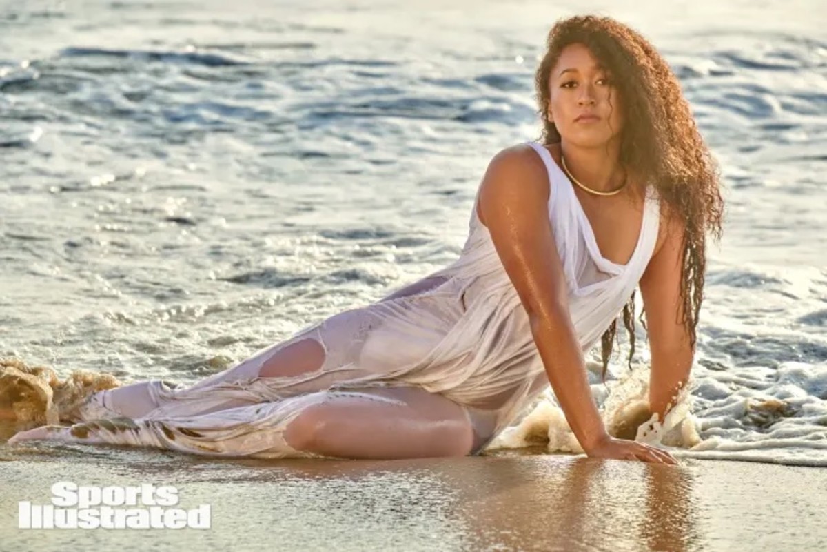 Naomi Osaka lays in the shallow water in a sheer white dress.