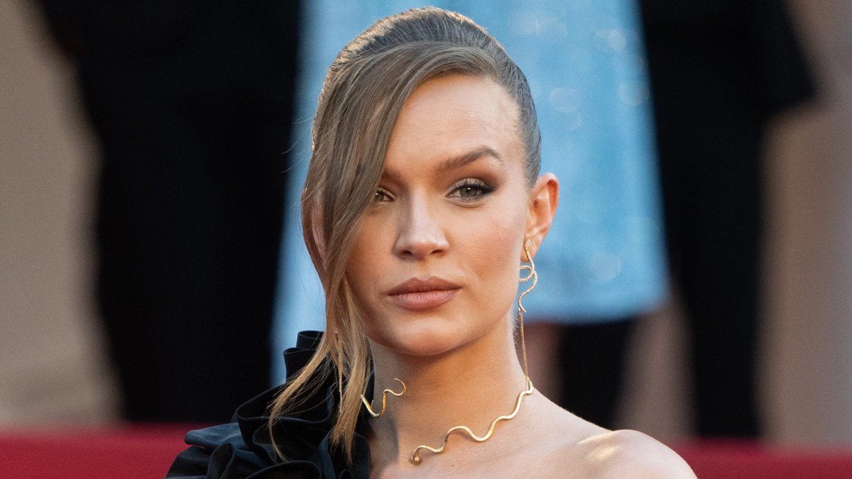 Josephine Skriver poses for the camera wearing a black one-shoulder dress and a gold choker necklace.