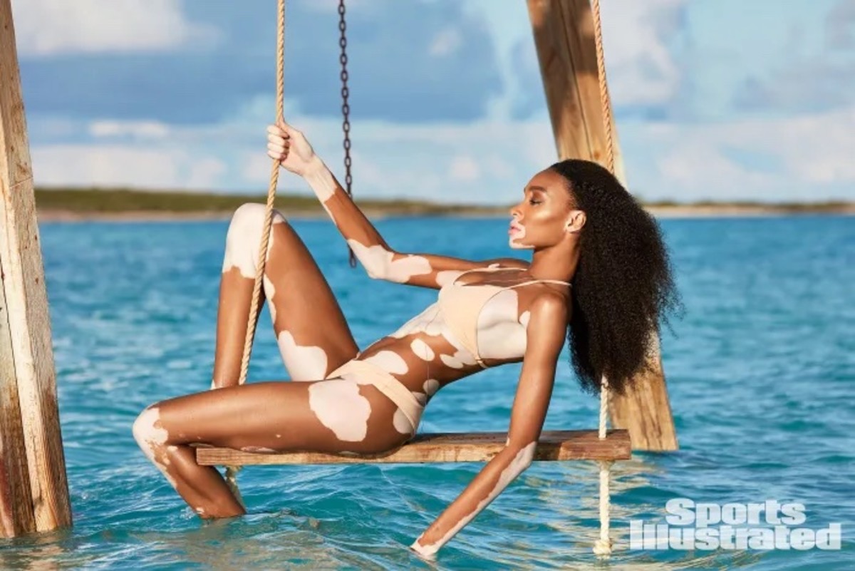 Winnie Harlow poses on a wooden swing over the ocean wearing a cream-colored bikini.