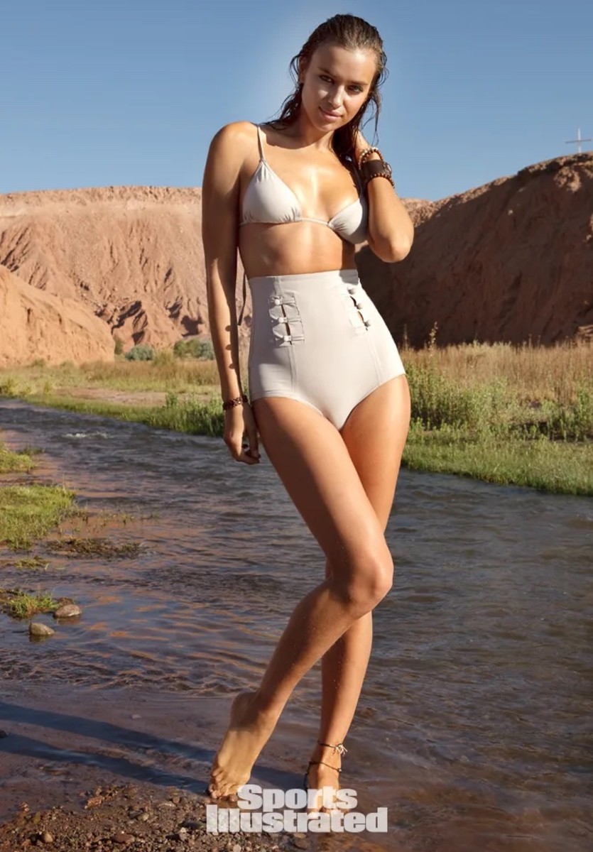 Irina Shayk stands in the shallow water of a desert creek and poses in a cream-colored triangle bikini and high-waisted bottoms.