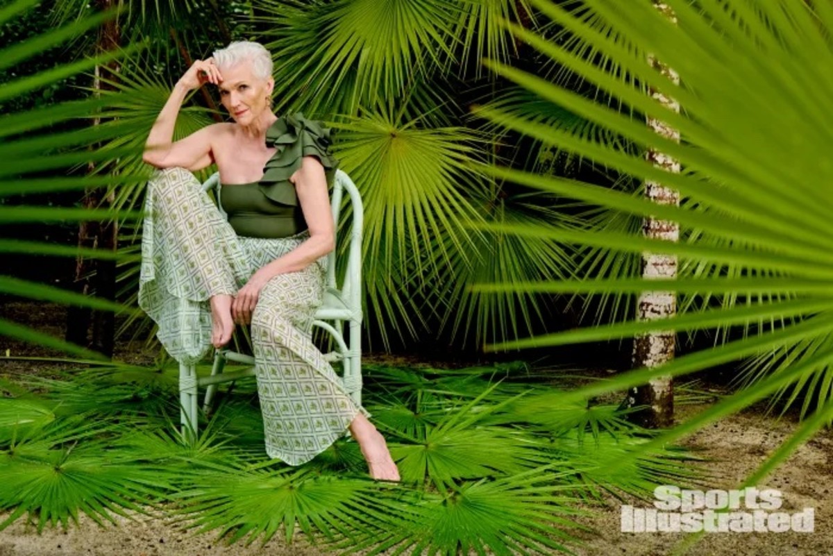 Maye Musk sits in a chair in front of green palm fronds in her green swimsuit and patterned pants.