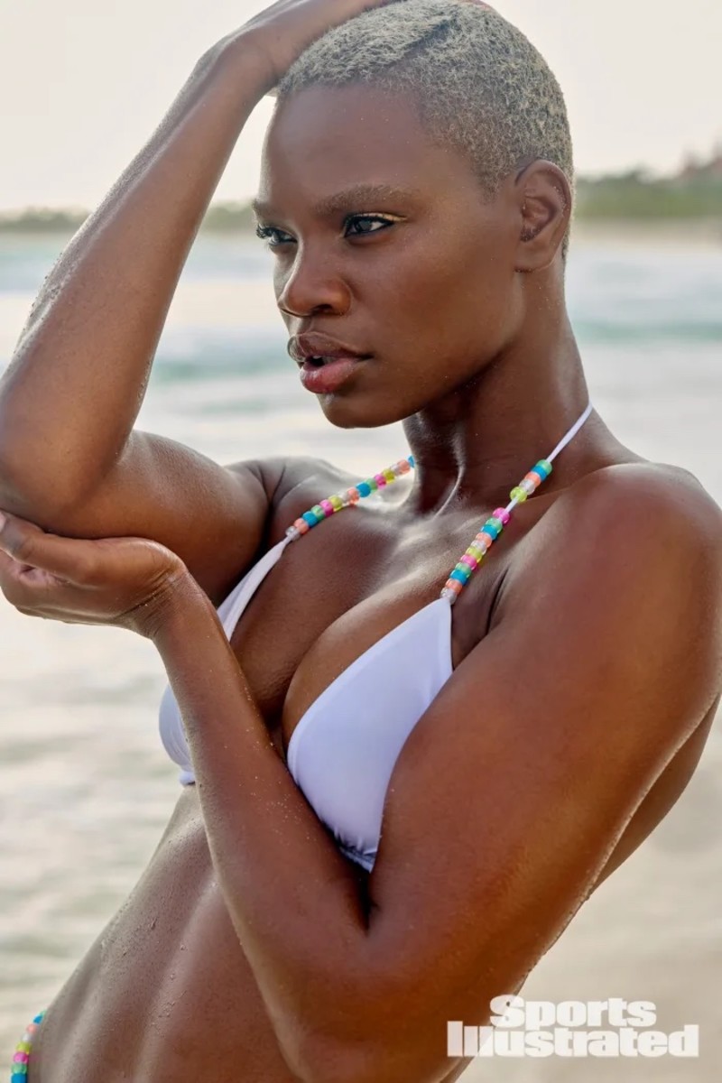 Ashley Byrd poses with her hand on her head in white bikini top with colorful beaded straps.