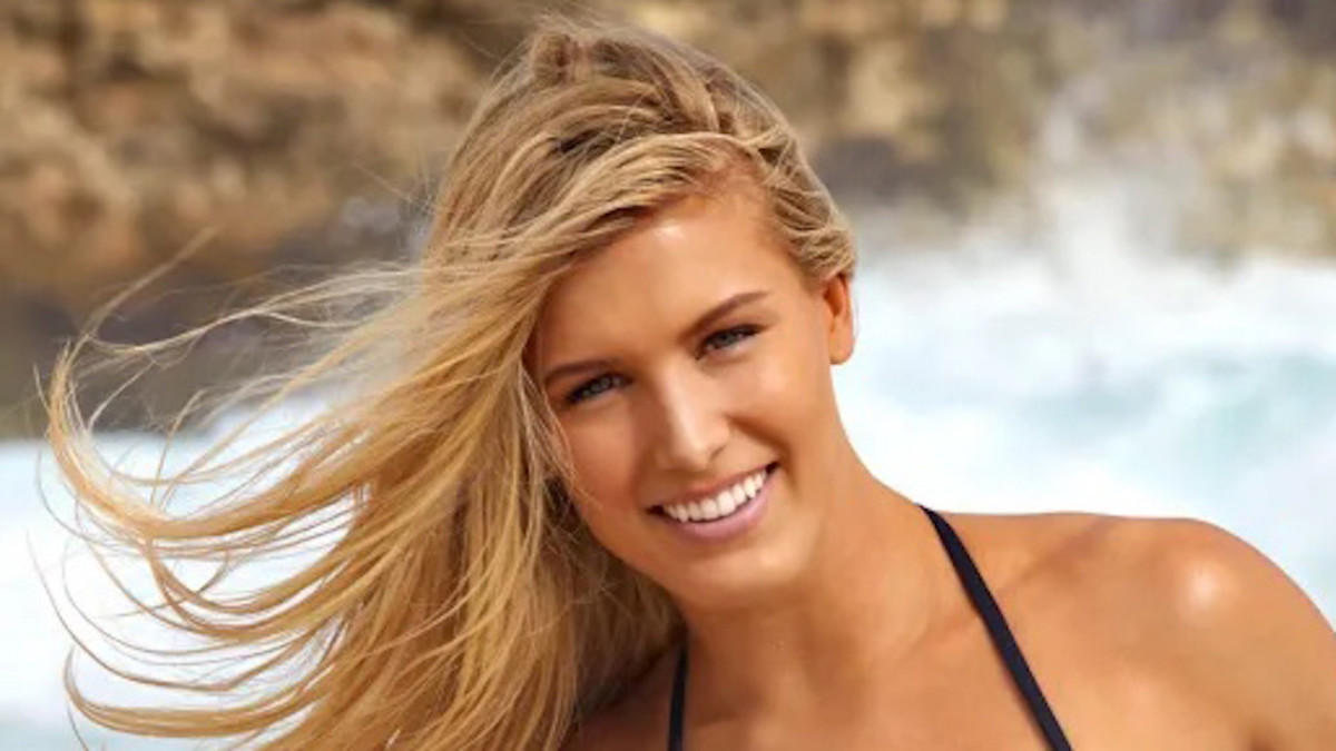 Genie Bouchard poses in front of the ocean in a black swimsuit.