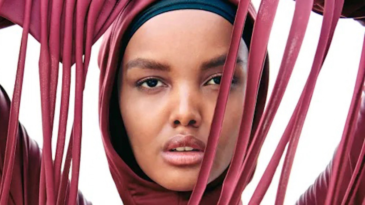 Halima Aden poses in berry pink hijab with long fringe hanging in front of her face.